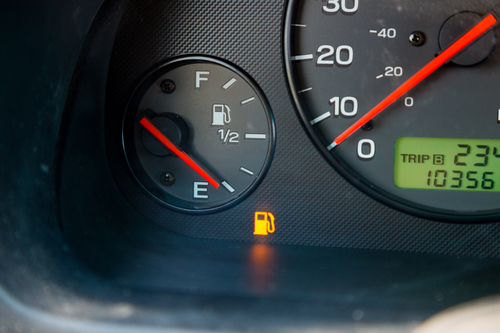 Gas Guage Empty A gas guage in a car reads empty and shows the warning light to let the driver know they are out of gas and need to refuel.
